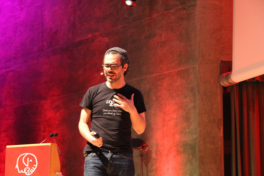 Marcello Duarte speaking on a conference stage lit in magenta and red
